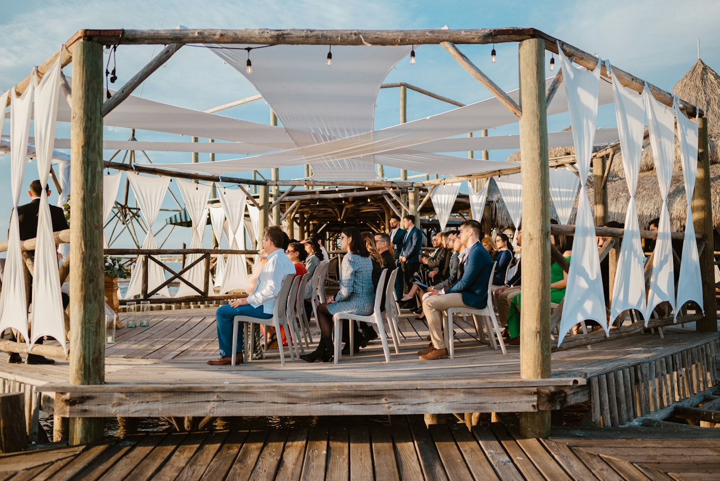 Wedding guests seated on a wooden deck under a fabric canopy