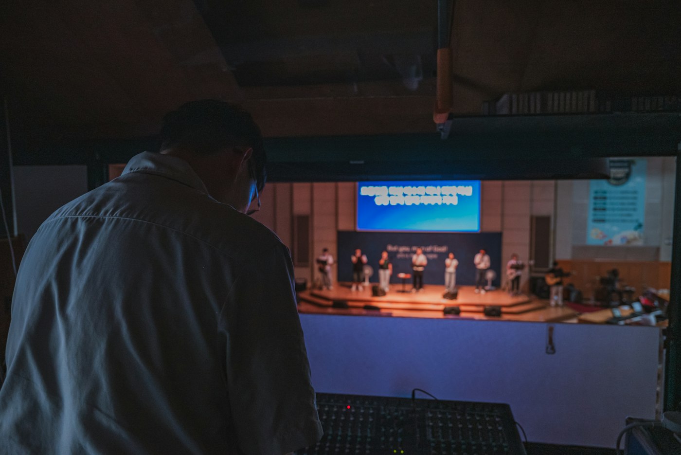 Sound technician at a mixing desk facing a worship stage